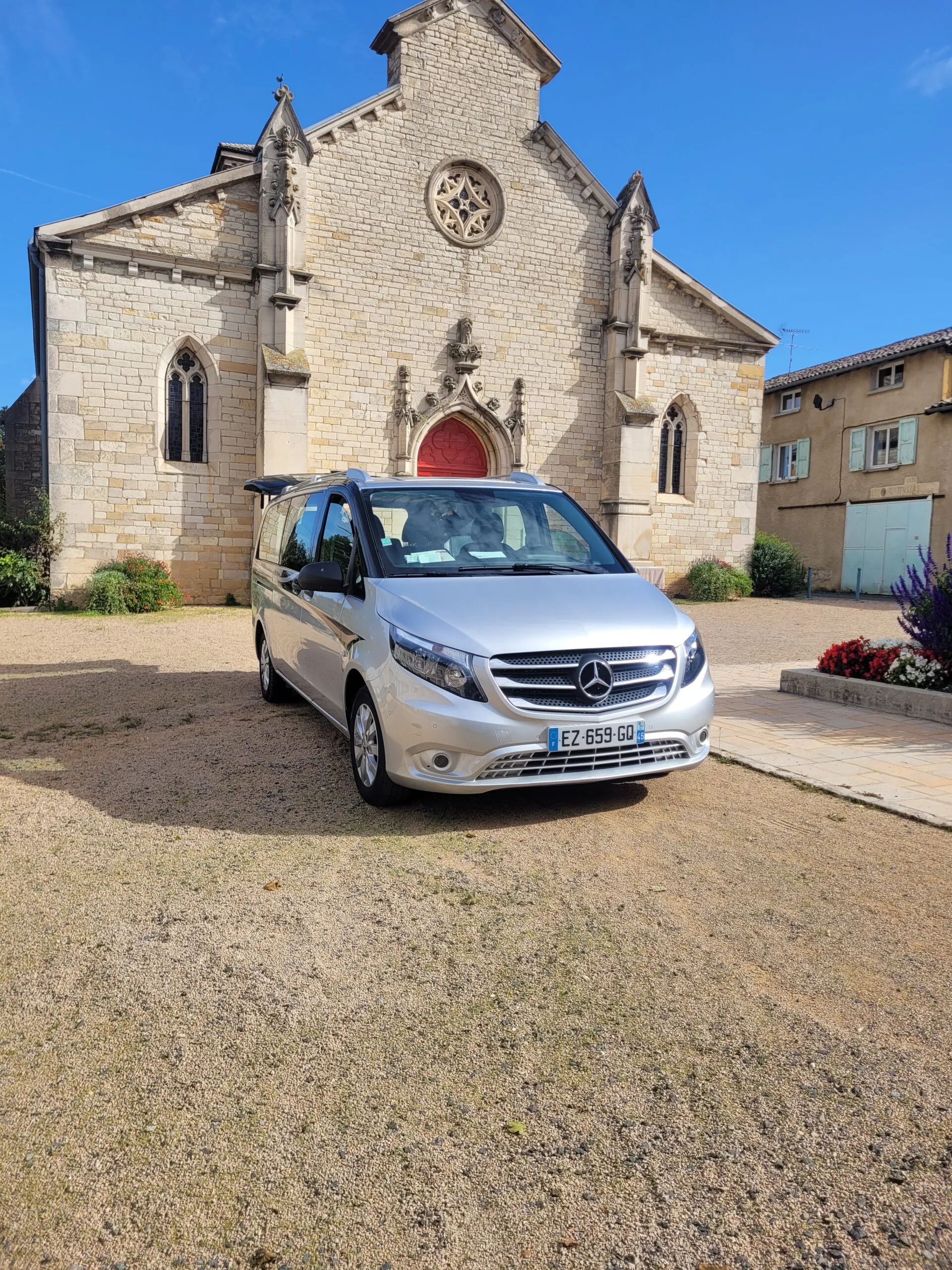Corbillard Mercedes argenté stationné devant une ancienne église en pierre.