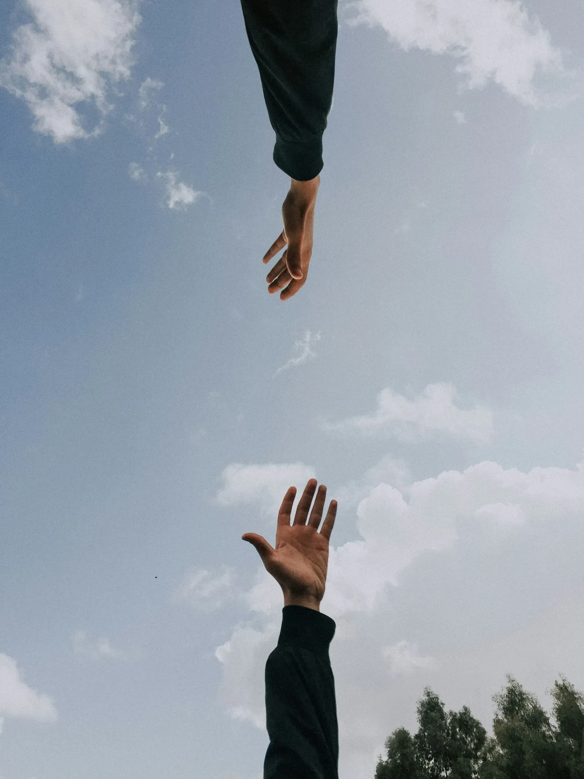 Deux mains s'étendant l'une vers l'autre sur fond de ciel nuageux.
